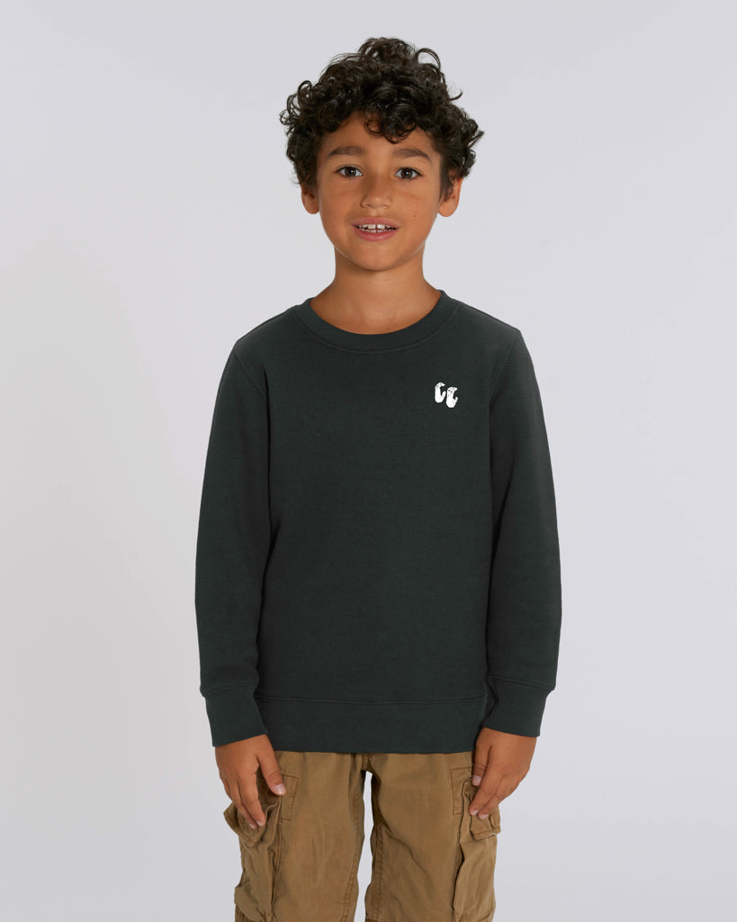 A young boy wearing a black crew neck sweater, styled with blue jean shorts. The sweater has a small white logo on the left chest position which is of two hands in a crimp climbing position