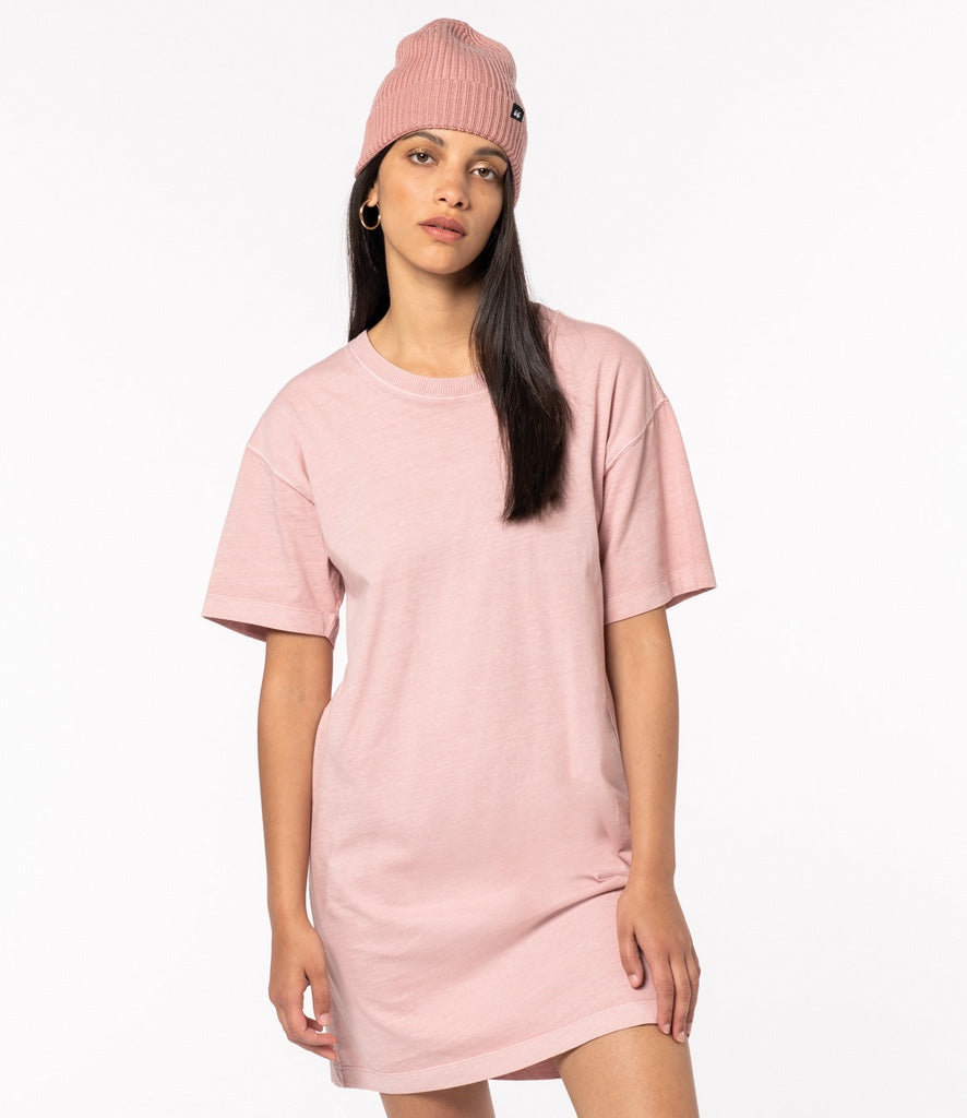 A woman wears a Crimpd Clothing soft pink beanie made from 100% merino wool. IT contrasts with her long dark hair and matches her casual pink t-shirt dress