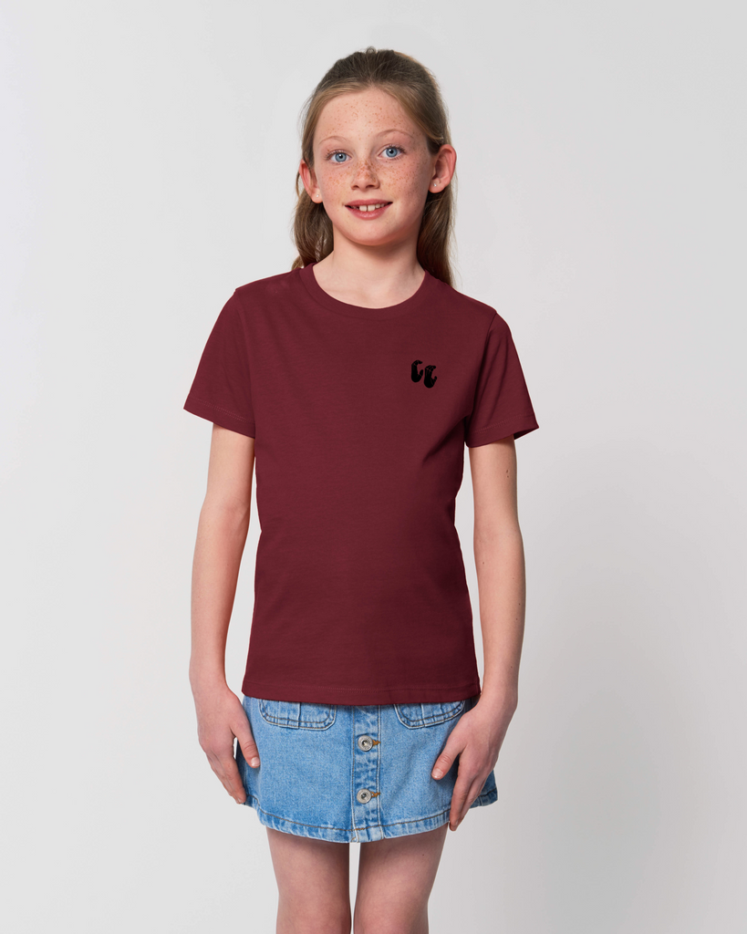 A girl wearing a kids organic cotton t-shirt in burgundy, with a printed black chest logo