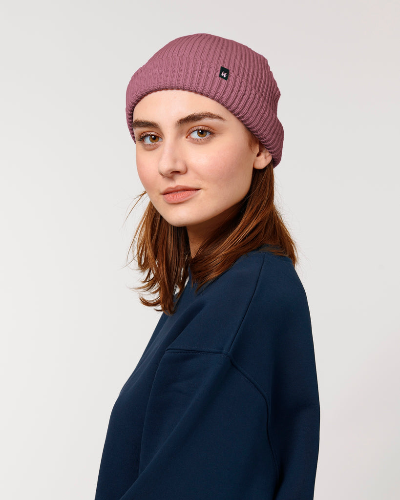 A woman wearing a dusky rose pink unisex fisherman's beanie hat made from organic cotton