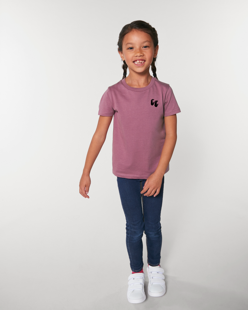 A girl wearing an organic cotton kids t-shirt in hibiscus pink, with a printed black left chest logo