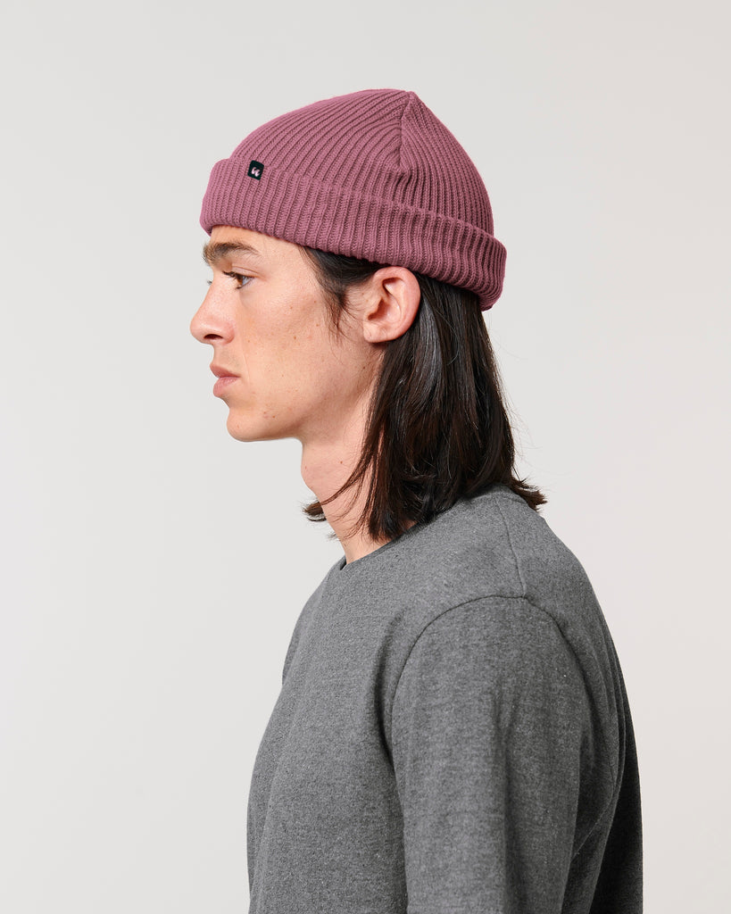The side view of a man wearing a dusky rose pink unisex fisherman's beanie hat made from organic cotton