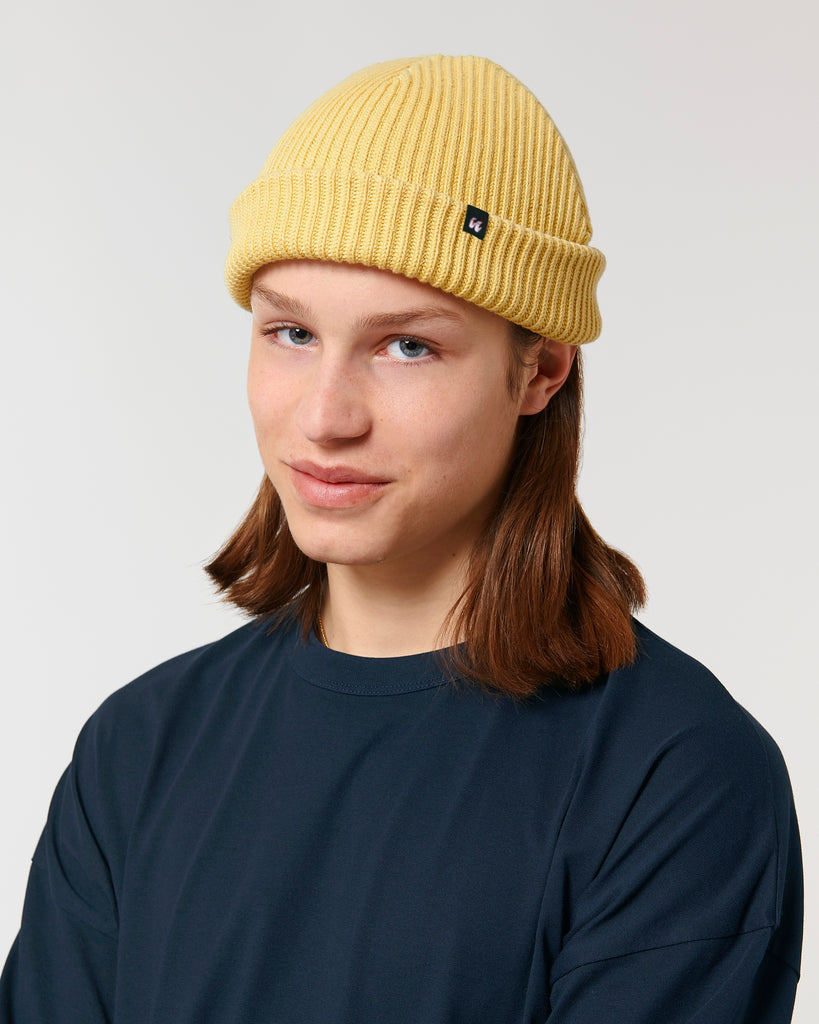 A man wearing a pastel yellow unisex fisherman's beanie hat made from organic cotton