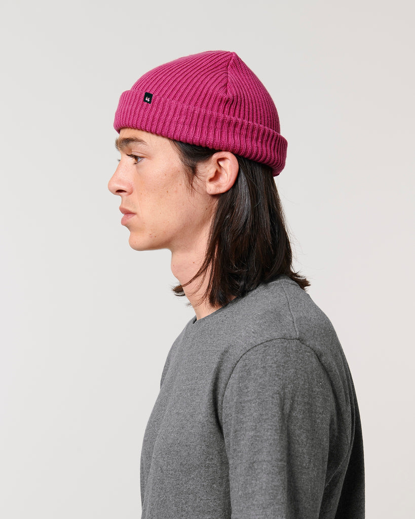 A man wearing a bright pink unisex fisherman's beanie hat made from organic cotton
