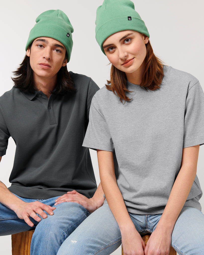 Two people sat together wearing mint green beanie hats, grey t-shirts and faded blue jeans.