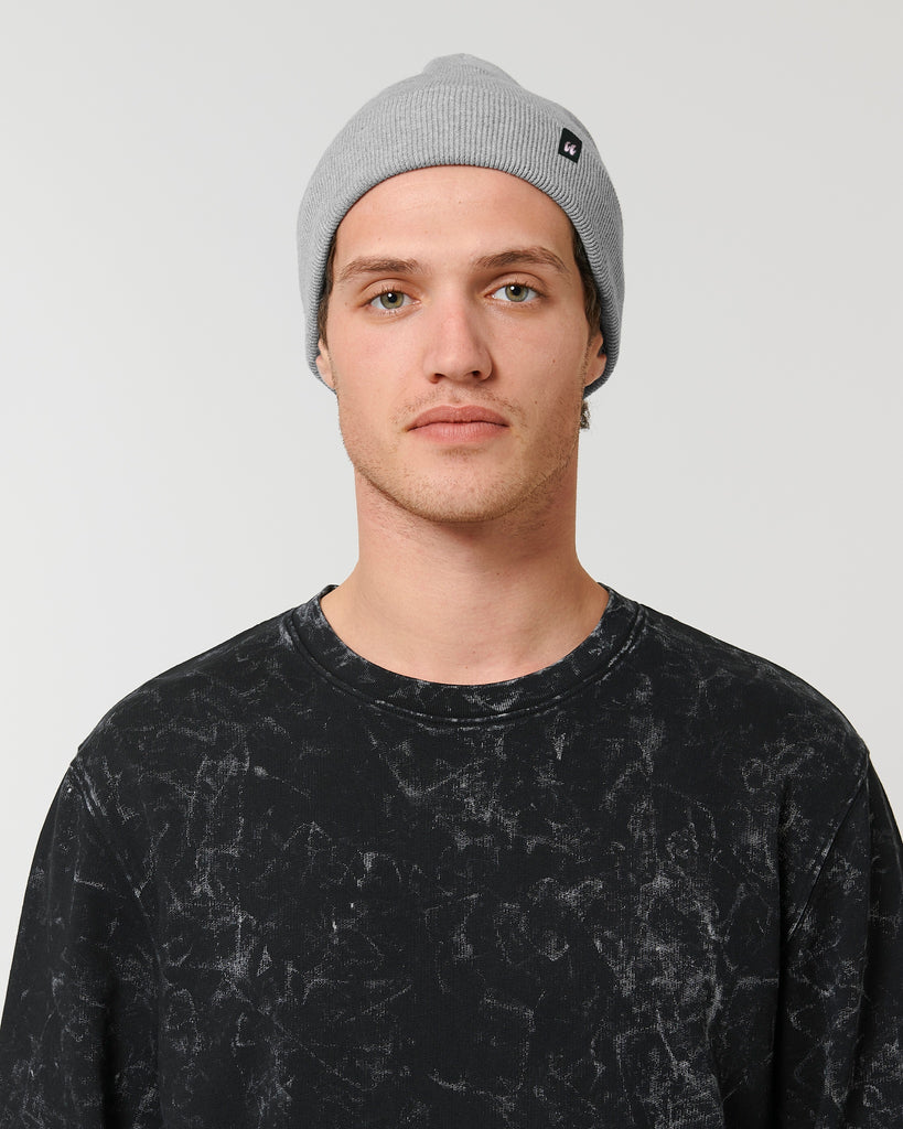 A person wearing a mid-grey beanie hat that has a small black fabric label stitched to the folded cuff