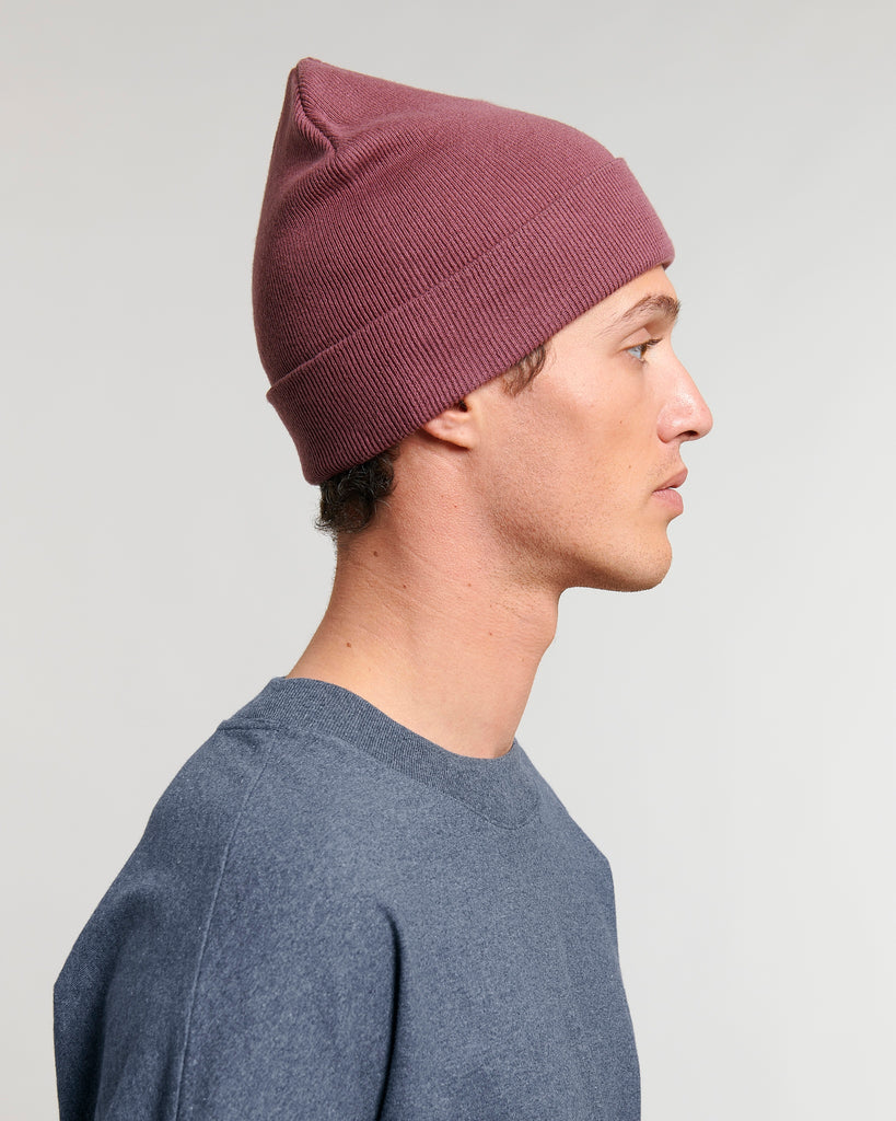 The side-view of a person wearing a dusky rose pink beanie hat and denim blue t-shirt