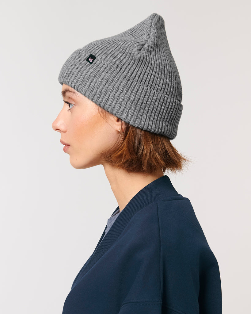 The side view of a woman wearing a mid heather grey unisex fisherman's beanie hat made from organic cotton