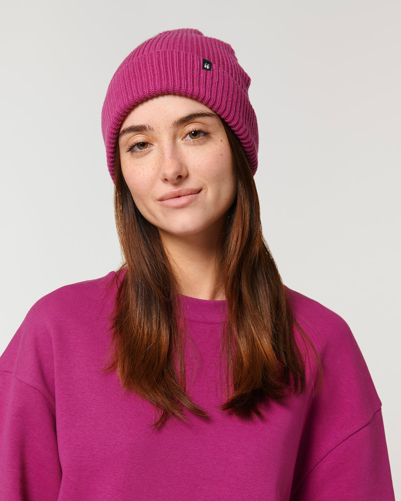 A woman wearing a bright pink unisex fisherman's beanie hat made from organic cotton